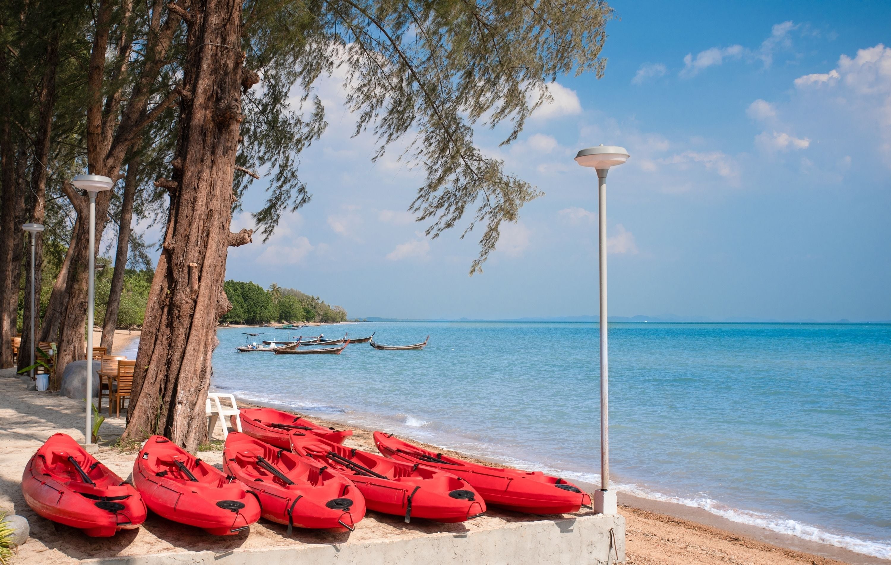 Une plage avec des kayaks rouges, une chaise blanche et un lampadaire.