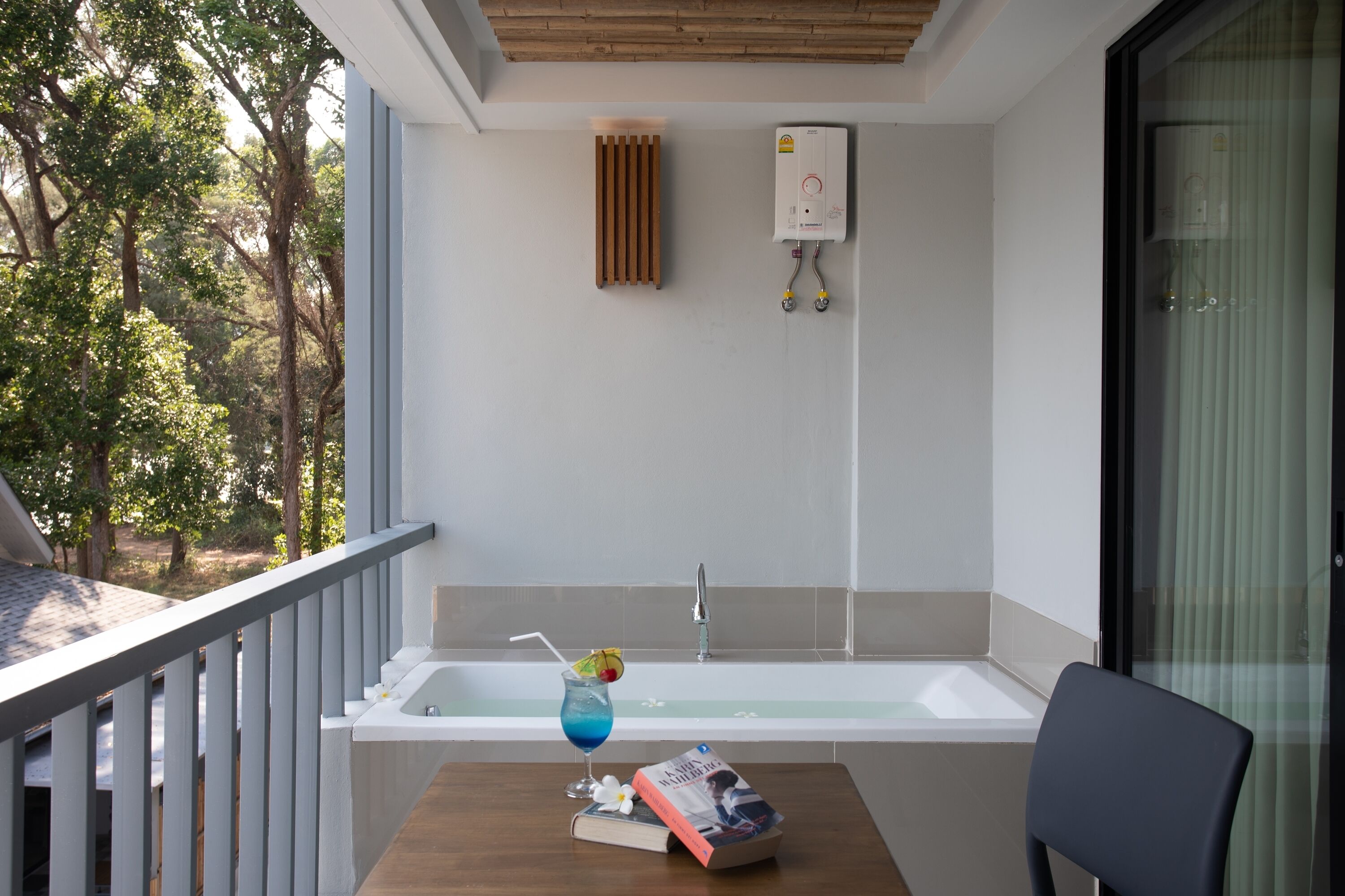 Un balcón con vistas a árboles, una bañera y un libro sobre una mesa.