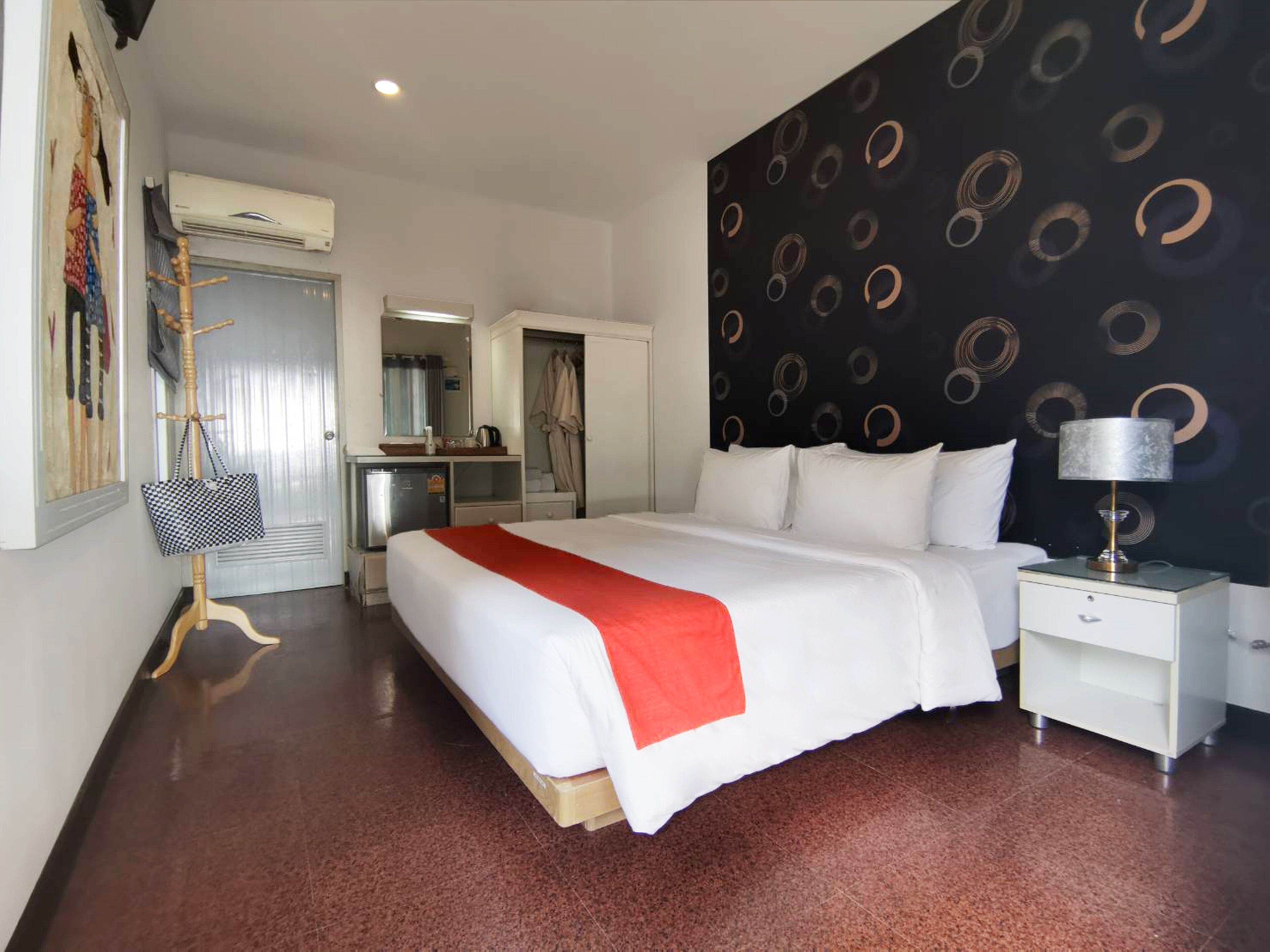 A hotel room with a large bed, a wardrobe, a desk, a mirror, and a bathroom visible through an open door.