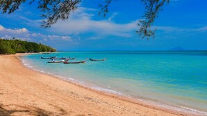Une plage avec une eau turquoise et limpide, plusieurs bateaux et une rive sablonneuse.