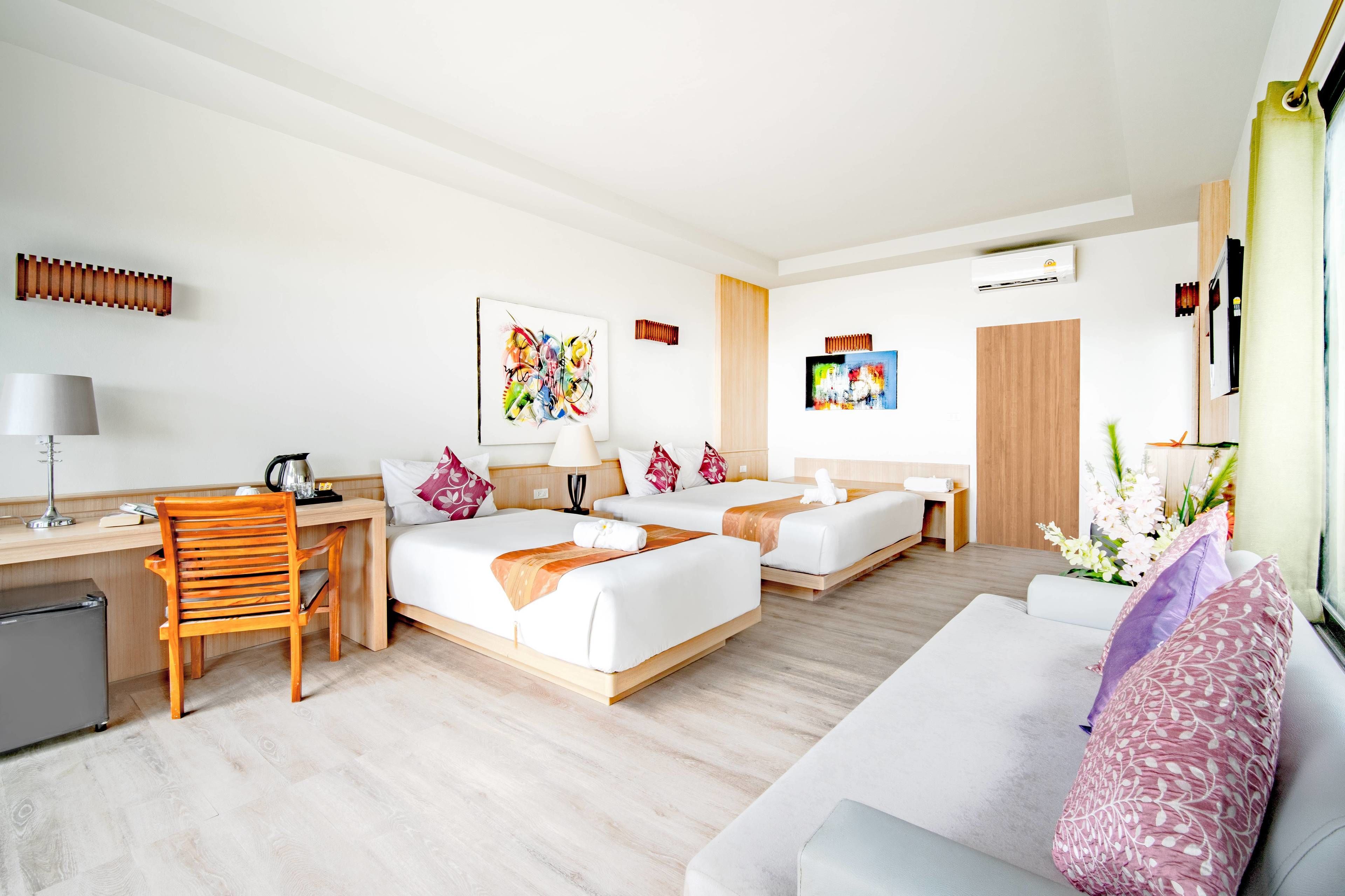 A hotel room with two beds, a desk, a chair, a sofa, and a TV.