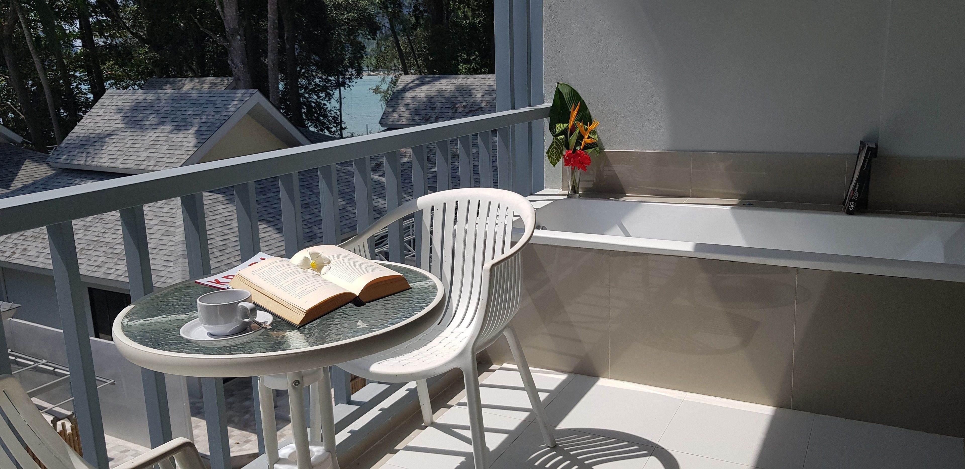 A balcony with a table and chairs, a book, a cup, and a vase with flowers.