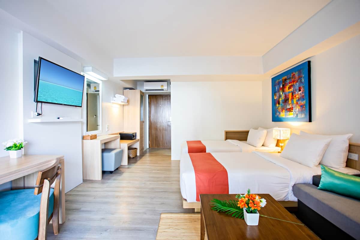 Een hotelkamer met een televisie, een bureau met stoel, een bed met kussens, een bank en een schilderij aan de muur.