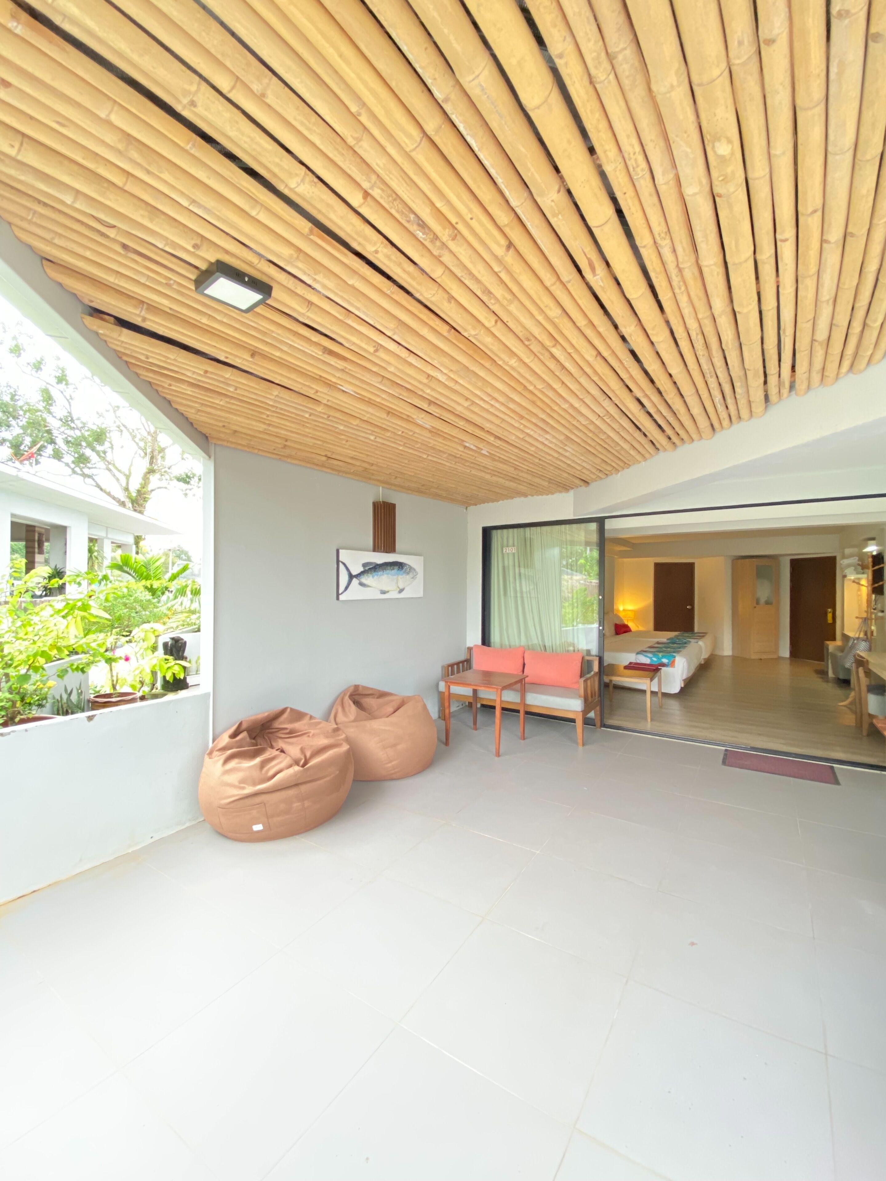 A modern interior with a bamboo ceiling, a dining area with a table and chairs, and a bed in the background.