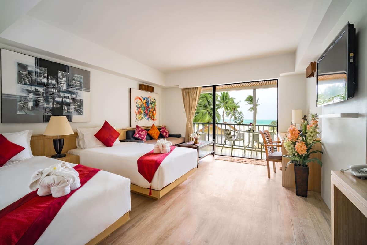 Hotelkamer met twee bedden, een balkon met uitzicht op palmbomen en een aan de muur bevestigde televisie.