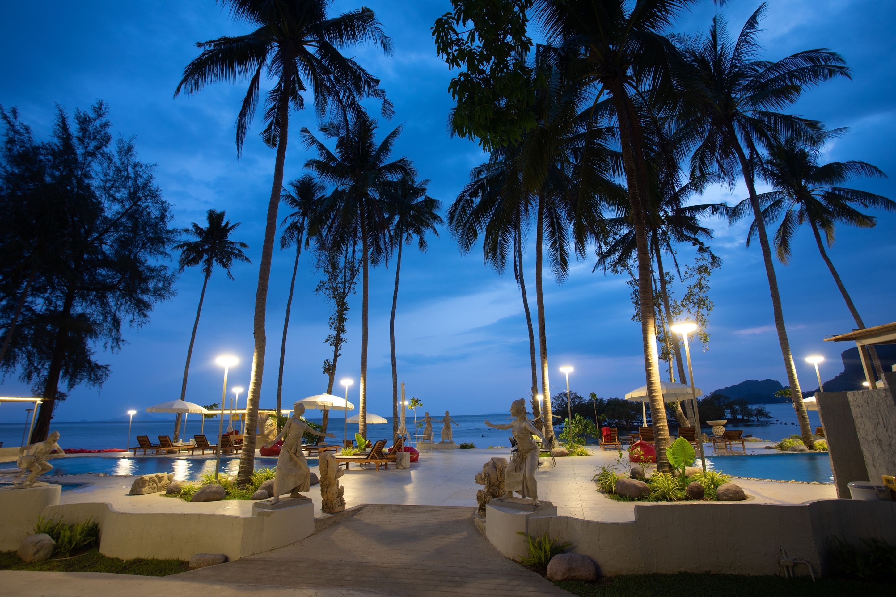 A resort pool area with palm trees, lounge chairs, and umbrellas at dusk.