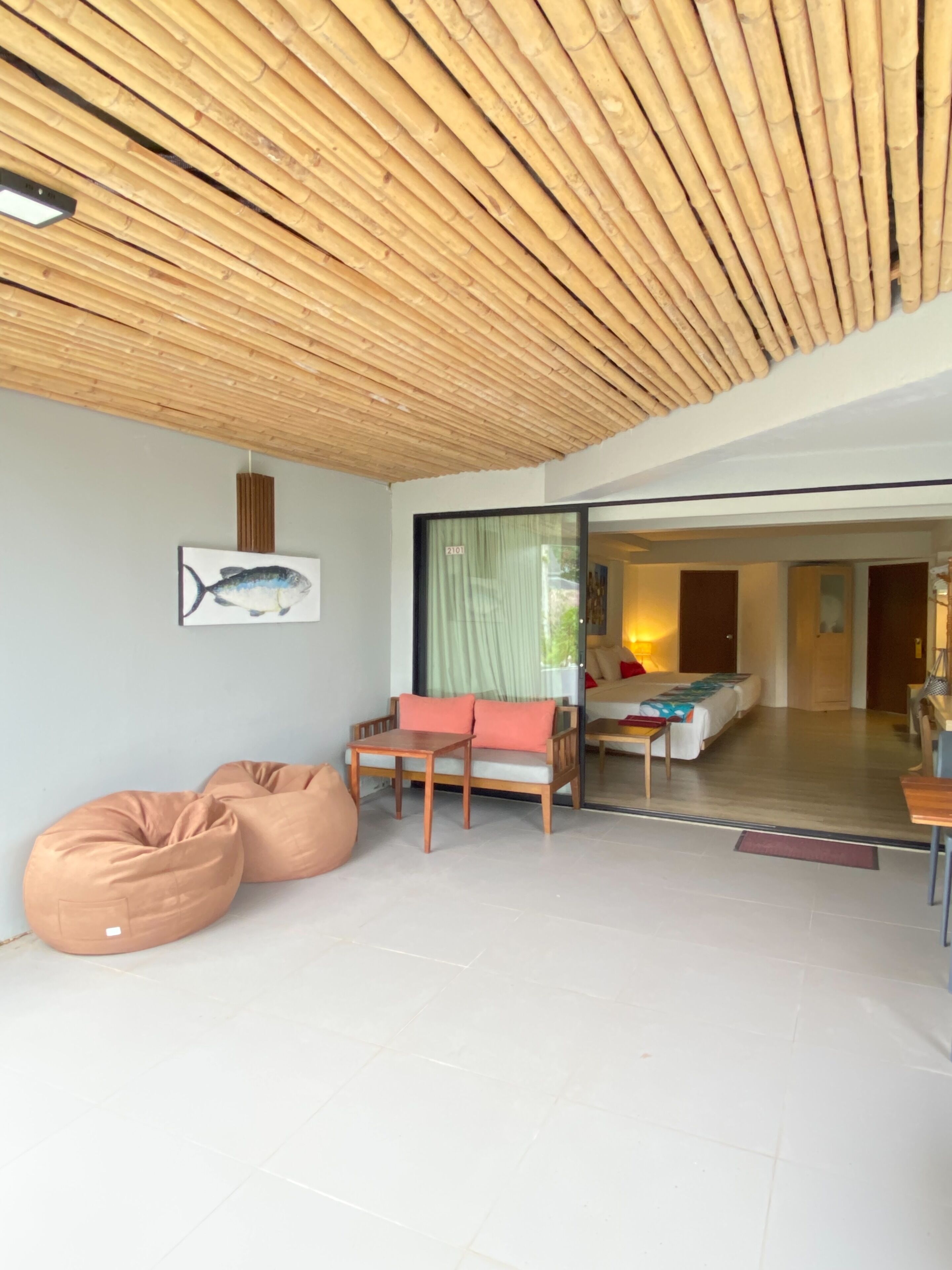 Un intérieur moderne avec un plafond en bambou, un canapé, un fauteuil en forme de poire et un lit en arrière-plan.