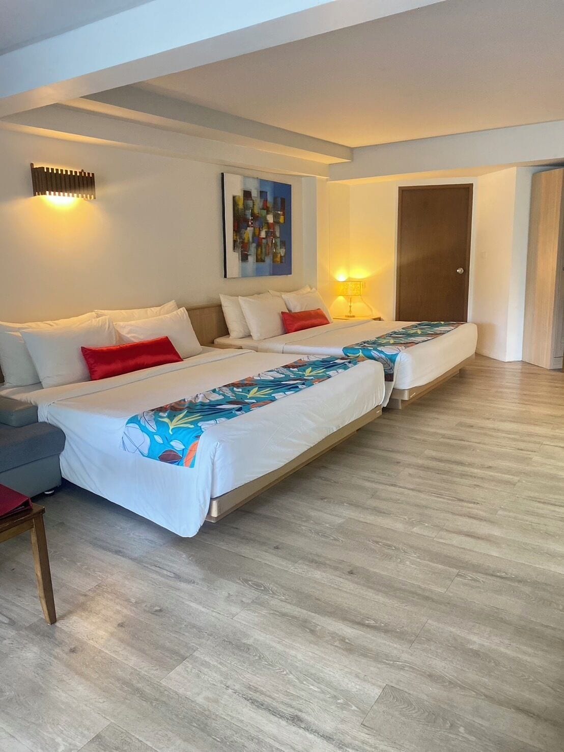 Quarto moderno com duas camas, um sofá e piso de madeira.