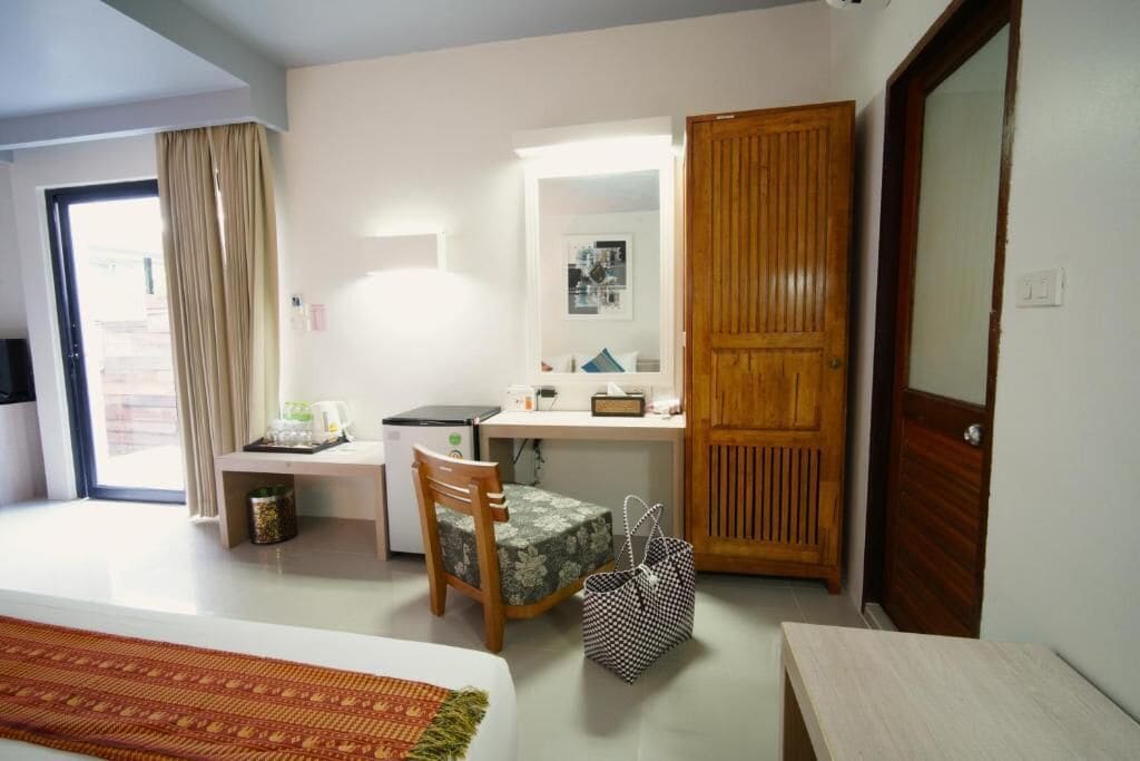 A hotel room with a bed, a desk, a chair, a wooden wardrobe, and a bathroom door.
