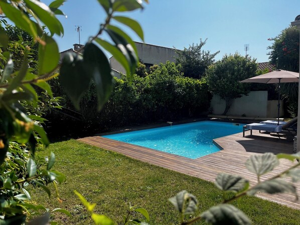 A backyard with a swimming pool, surrounded by greenery and a wooden deck.
