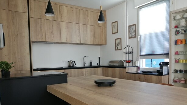 A modern kitchen with wooden cabinets, a black countertop, and pendant lighting. - Charming apartment, everything on foot or by bike. Heart of Capbreton (Capbreton)