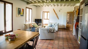 Uma sala ampla com uma mesa de jantar de madeira, dois sofás, uma televisão e uma cozinha com geladeira.