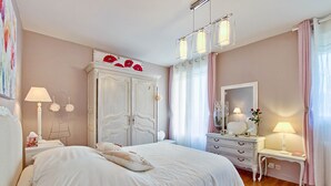 Quarto com uma cama grande, um guarda-roupa, uma penteadeira com espelho e uma mesa de cabeceira com abajur.