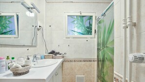Casa de banho com lavatório branco, espelho e chuveiro.