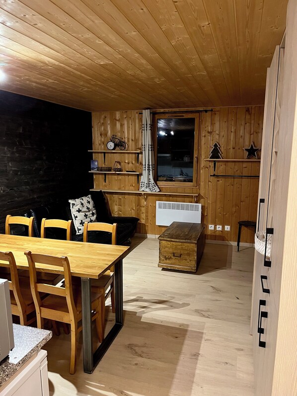 En ombonad träinredning med en matplats, en soffa, ett fönster med utsikt och en liten hylla med dekorativa föremål.