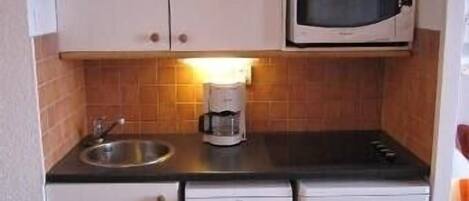 A compact kitchen with white cabinets, a microwave, a coffee maker, and a dishwasher.