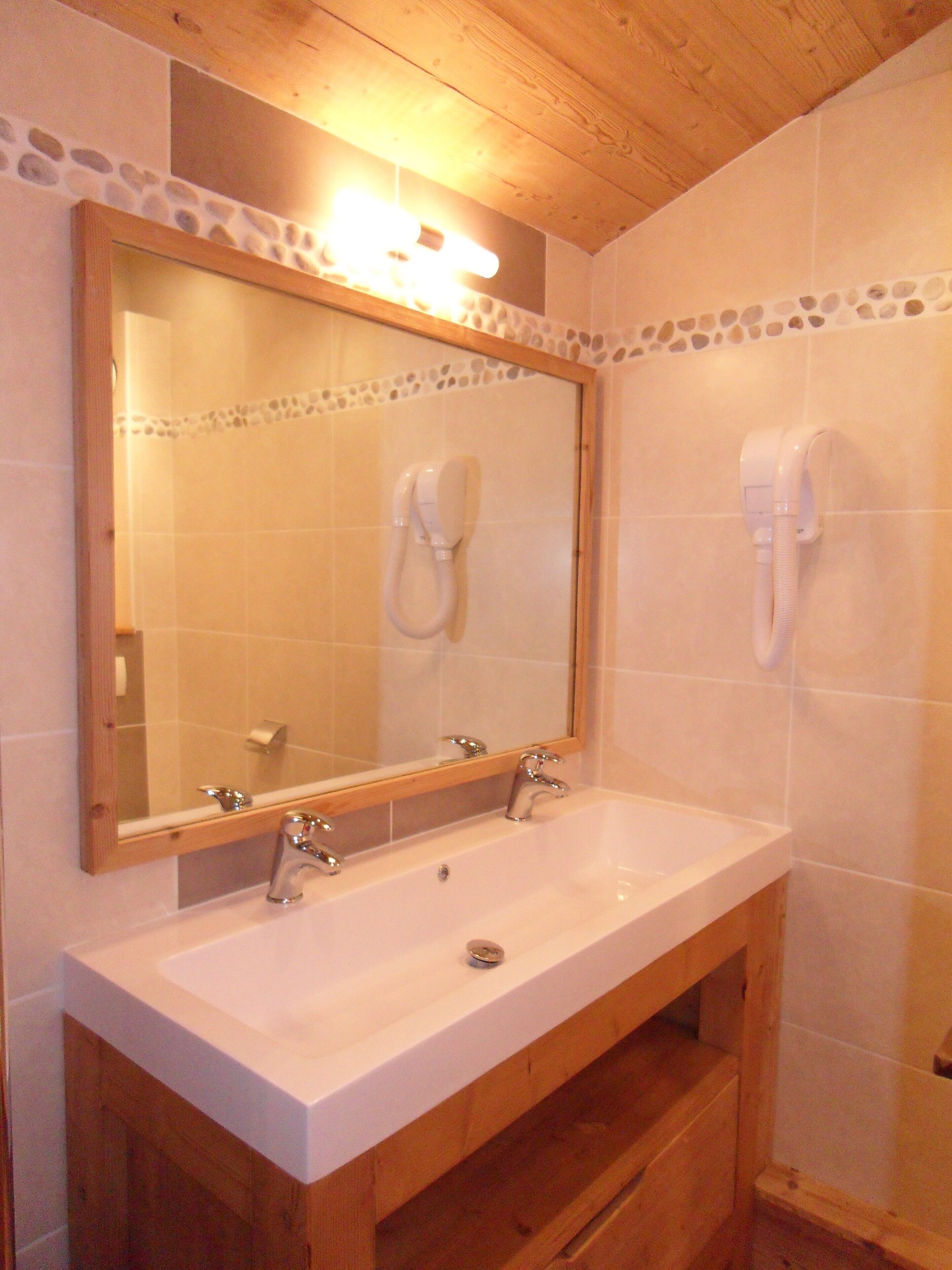 Un bagno con un mobile bagno in legno, uno specchio grande, due asciugacapelli a parete e un pavimento piastrellato.