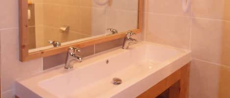 Un bagno con un mobile bagno in legno, uno specchio grande, due asciugacapelli a parete e un pavimento piastrellato.