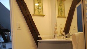 Un baño con techo de vigas de madera, un lavabo con espejo y dos luces empotradas.