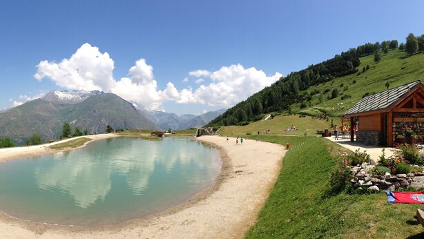 A lakeside resort with a wooden cabin, picnic areas, and a clear view of mountains.
