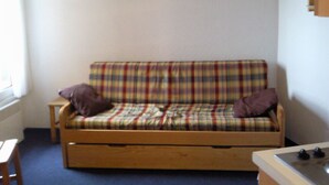 A small room with a plaid sofa, a wooden table, and a clock on the wall.