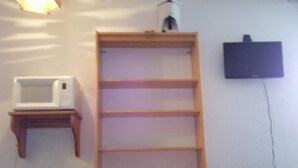 A room with a wooden table, a white microwave on a shelf, and a television mounted on the wall.