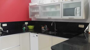 Une cuisine avec des meubles blancs, un plan de travail noir et un mur d’accent rouge.