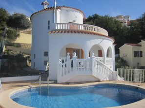 En hvid bygning med en pool, der har en balkon og en trappe til indgangen.