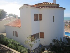 Ein weißes Gebäude mit rotem Ziegeldach, einem kleinen Balkon und Blick auf das Meer.