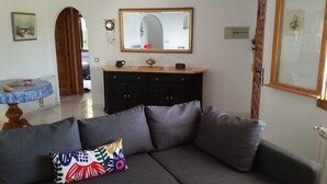 Un salon avec un canapé gris, un coussin coloré, un meuble en bois, une petite table et un miroir au mur.