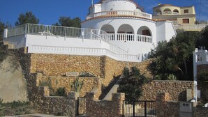 Un bâtiment blanc avec un socle en pierre, un balcon et un escalier menant à l’entrée.