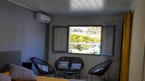 Ein Schlafzimmer mit einem Bett, zwei Stühlen, einem Fenster mit Vorhängen und einer Deckenleuchte.