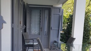 Ein überdachter Außenbereich mit Korbmöbeln und einem Glastisch, der zu einer Tür mit Milchglasfenster führt.