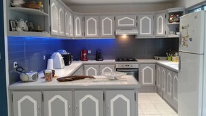 Eine Küche mit weißen Schränken, einer blauen Spritzschutzwand und verschiedenen Geräten, darunter eine Kaffeemaschine, ein Toaster und ein Kühlschrank.