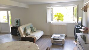 A well-lit living room with a sofa, a coffee table, and a TV stand. - 50m² studio with garden near Toulouse (Baziège)
