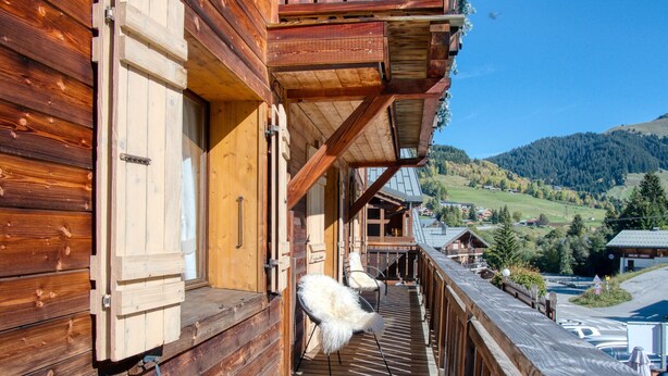 Una cabaña de madera con terraza de madera, un sillón blanco y mullido, y vistas a un valle.