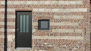 Ein Gebäude aus Ziegelsteinen mit einem Ziegeldach, einer schwarzen Tür und einem kleinen Fenster.