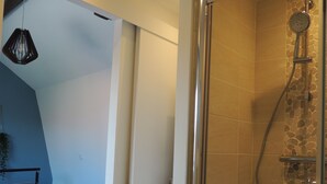 Ein modernes Badezimmer mit einer Duschkabine aus Glas, einem Bett mit gemusterten Betttextilien und einer Wand in Blautönen.