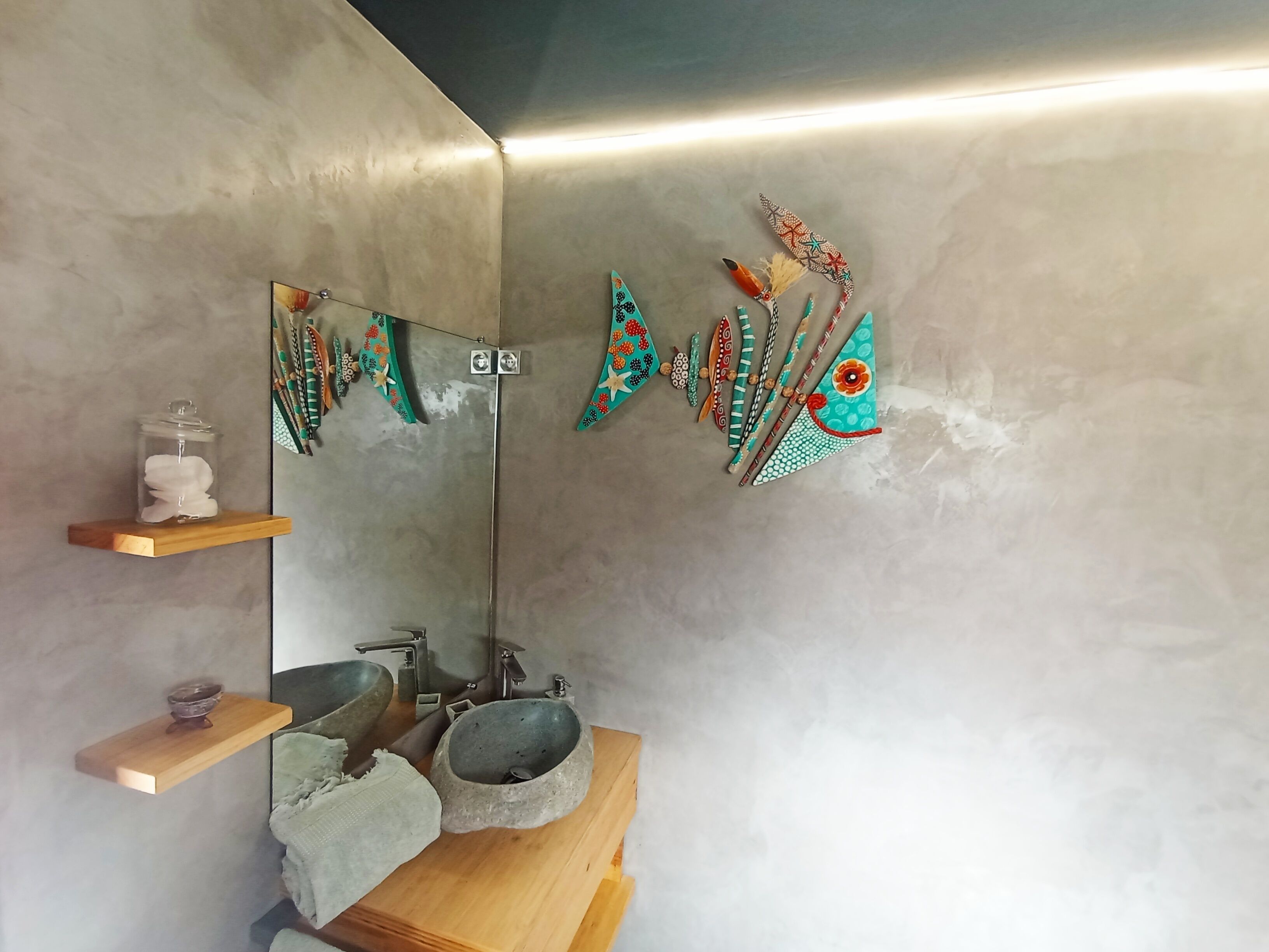 A bathroom with a stone sink, wooden shelves, and a mirror with decorative items.