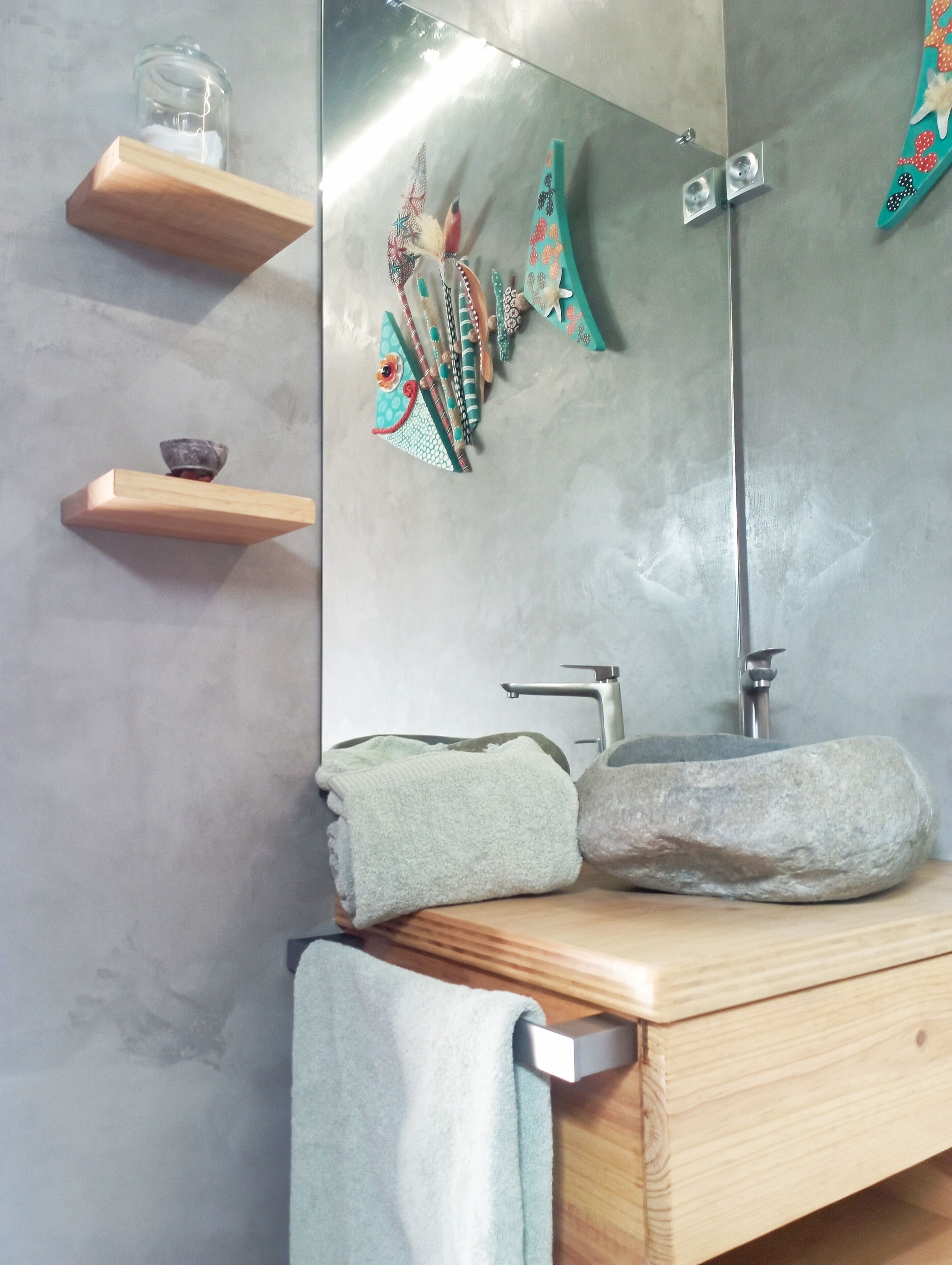 Une salle de bain avec un lavabo en pierre, des étagères en bois et un miroir.