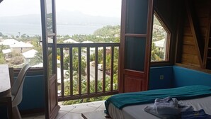Een slaapkamer met een bed, een bankje, een stoel en uitzicht op zee en heuvels.