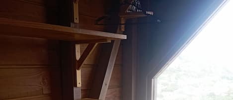 Un escritorio de madera con una silla, una ventana con vistas a follaje verde, y una pared azul.