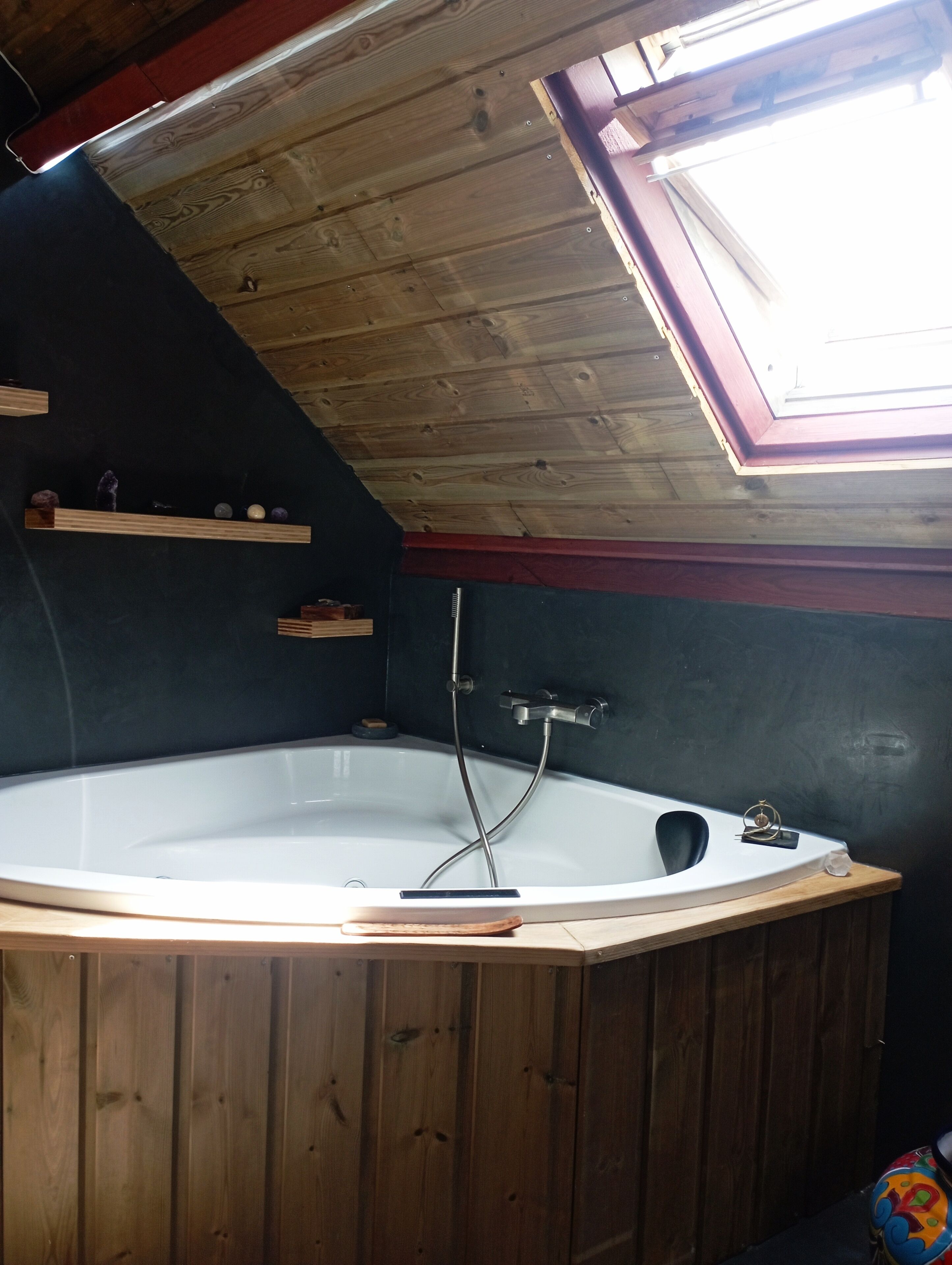 A wooden room with a skylight, a bathtub, and shelves with items.