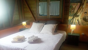 Een net opgemaakt bed met witte lakens en kussens, twee nachtlampen en een schilderij van een giraffe en een struisvogel aan de muur.