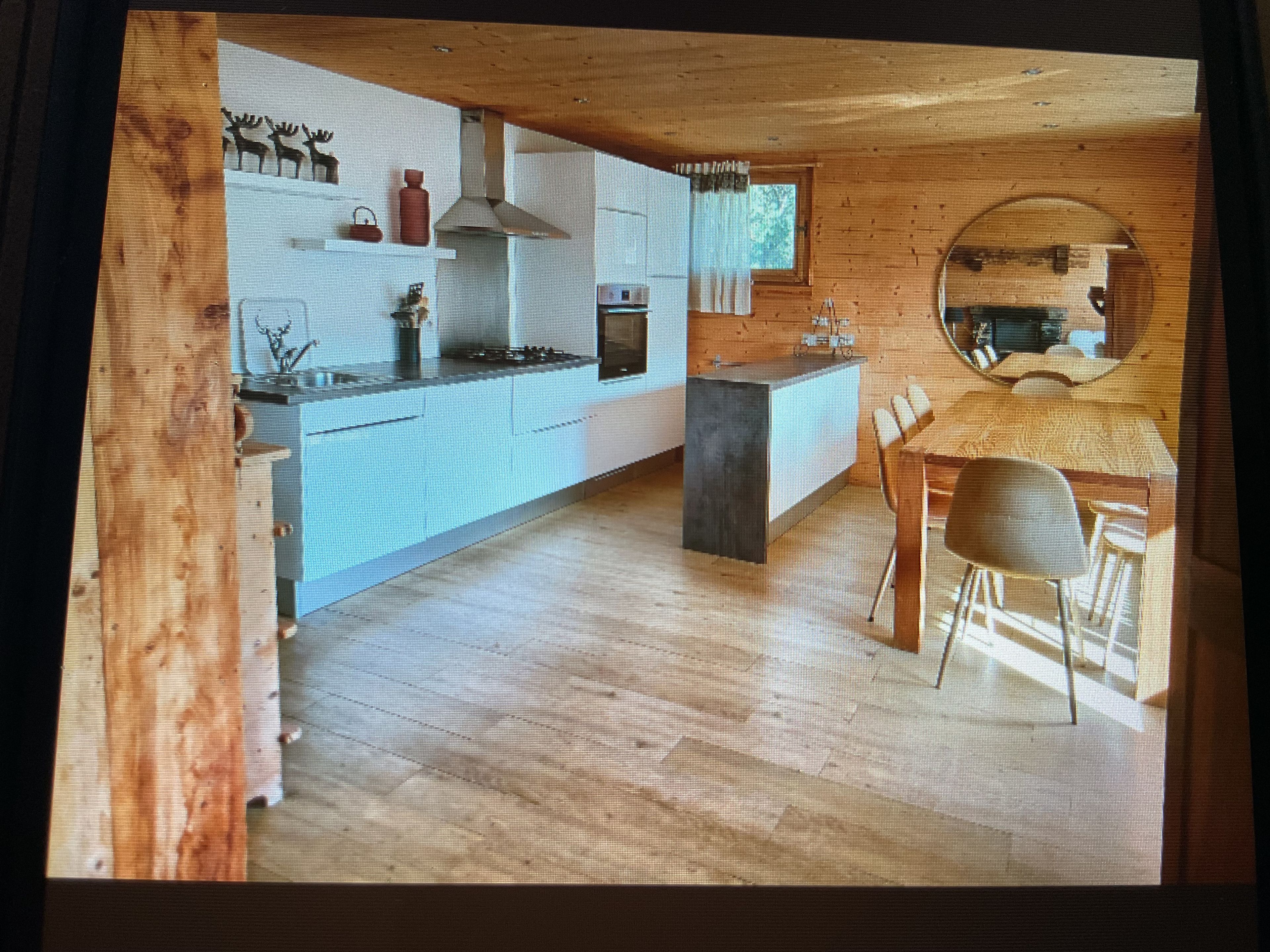Una cocina moderna con una isla central, suelo de madera y un comedor con un espejo redondo.