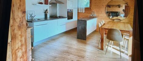 Una cocina moderna con una isla central, suelo de madera y un comedor con un espejo redondo.