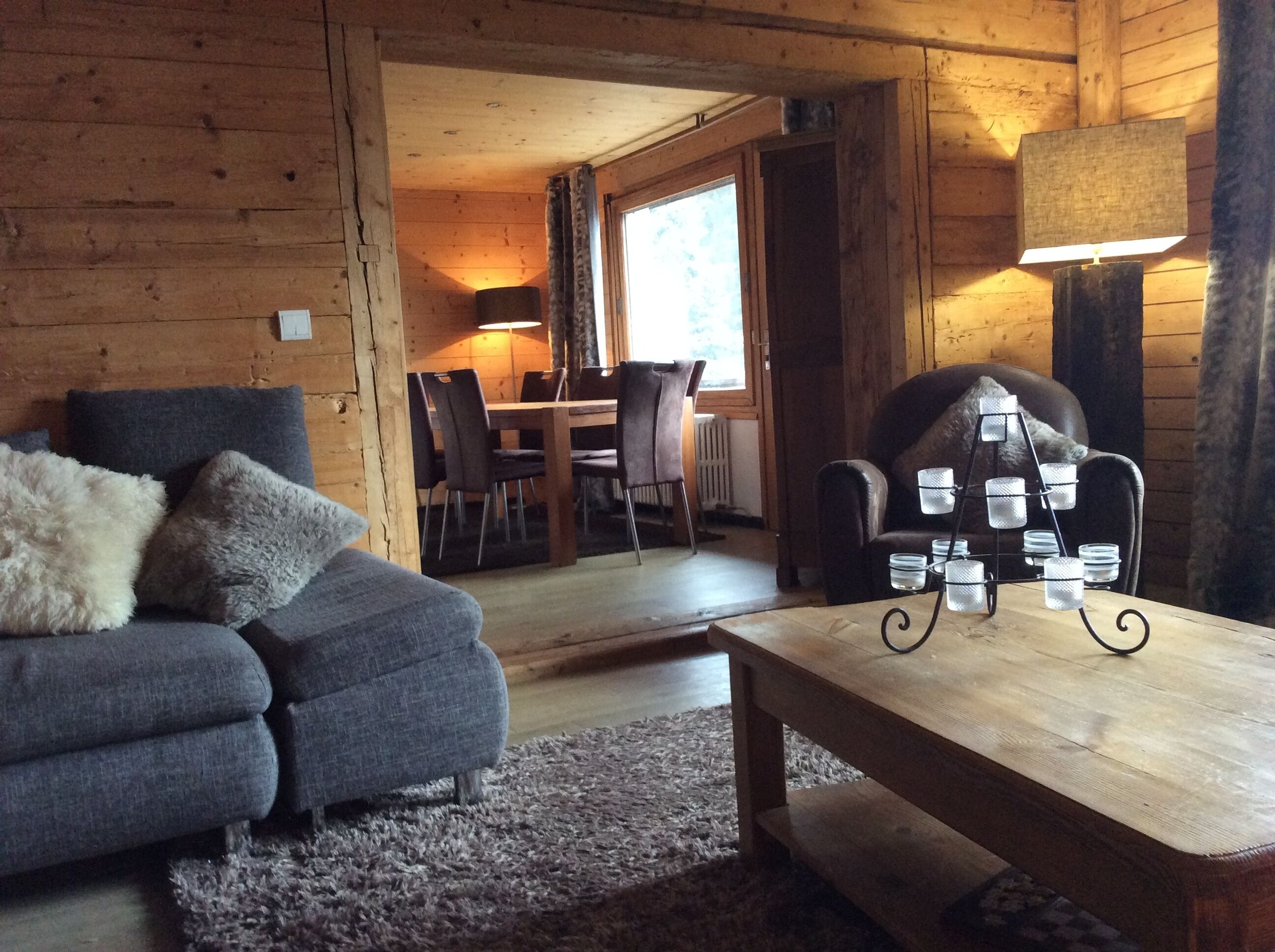 A cozy log cabin interior with a sofa, a dining table with chairs, and a lamp.