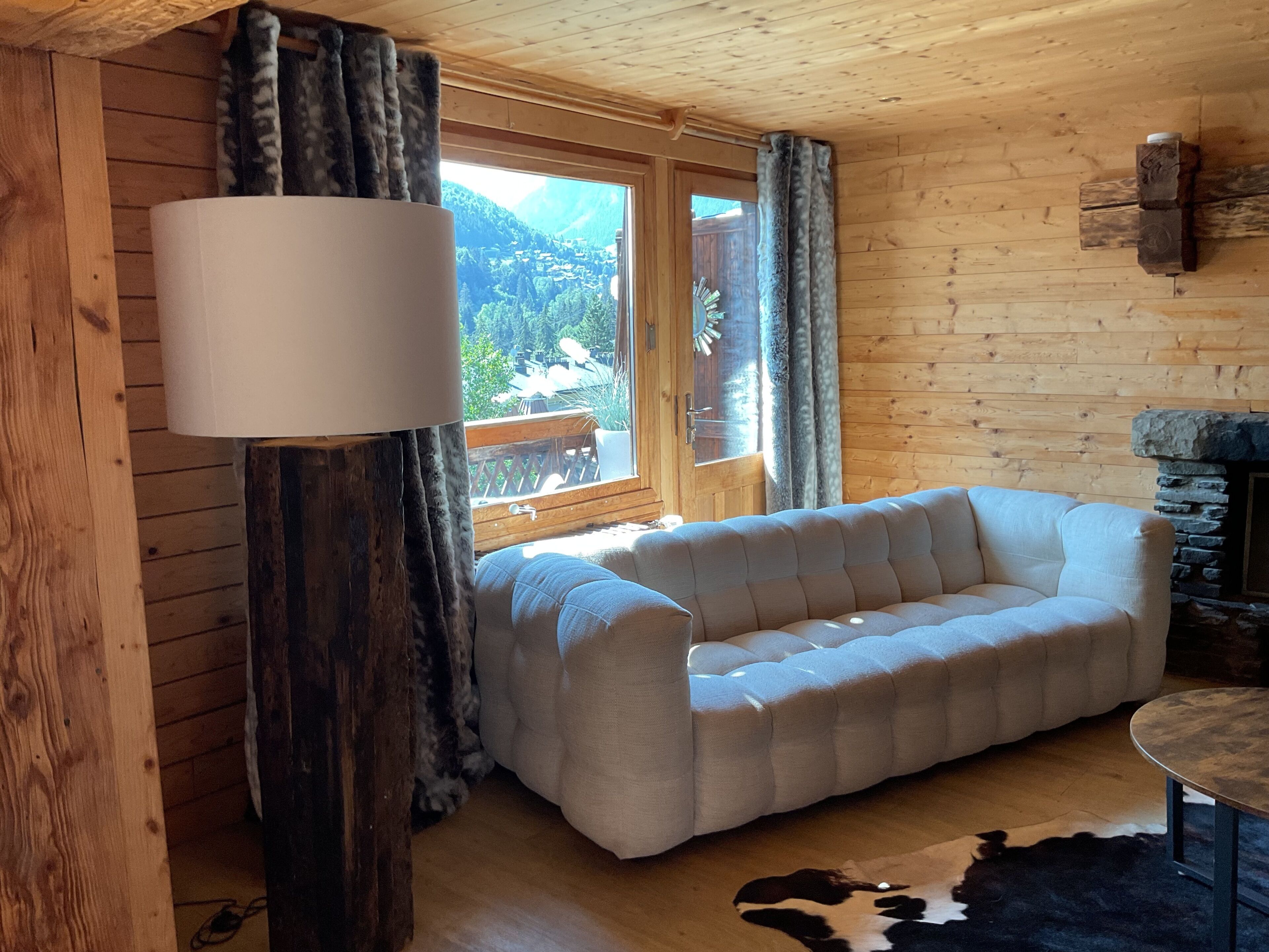 A cozy room with a sofa, a lamp, a stone fireplace, and a view of the outdoors.