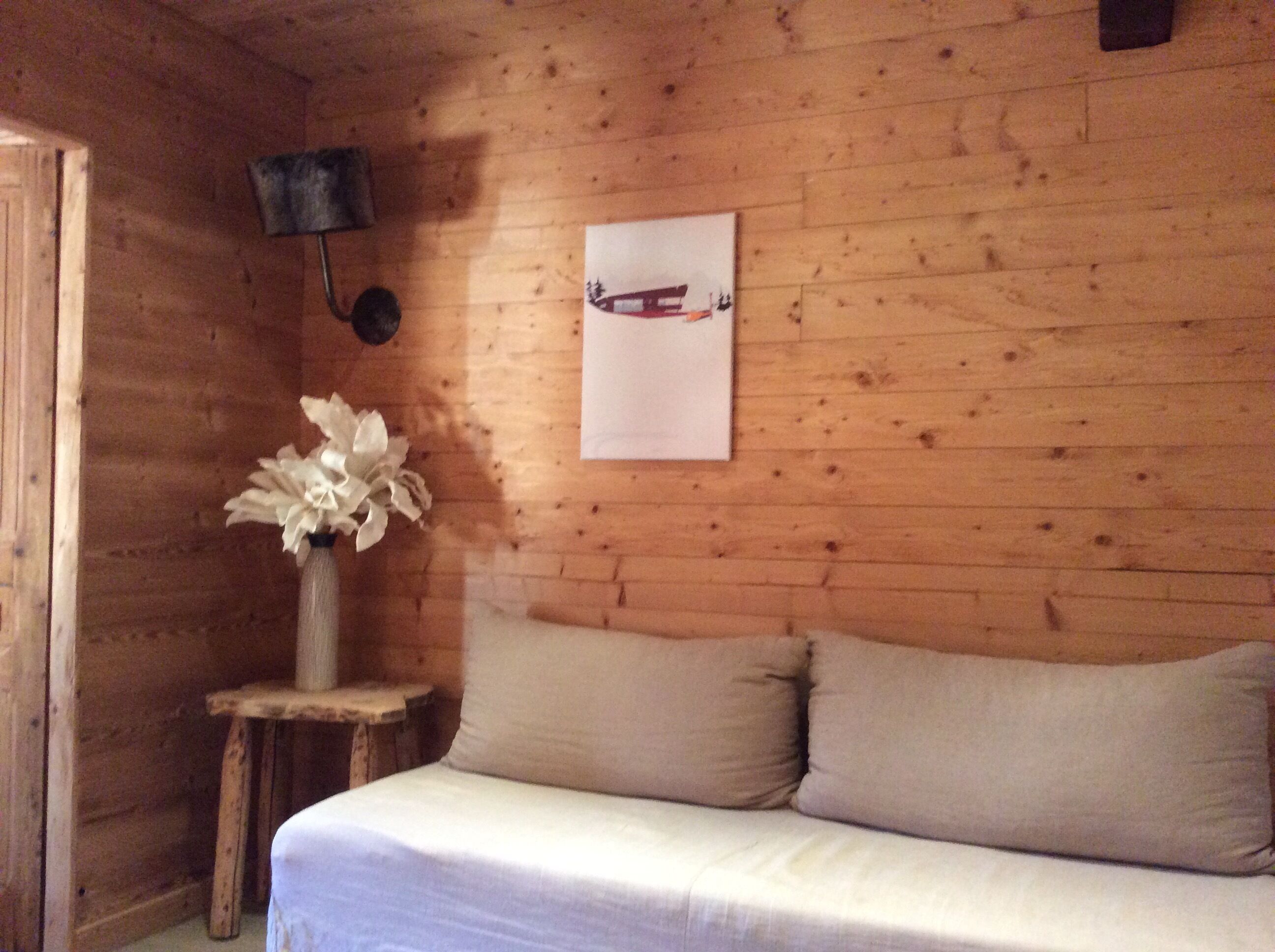 Une pièce de cabane en bois comprenant un lit, une petite table avec un vase de fleurs et une lampe fixée au mur.