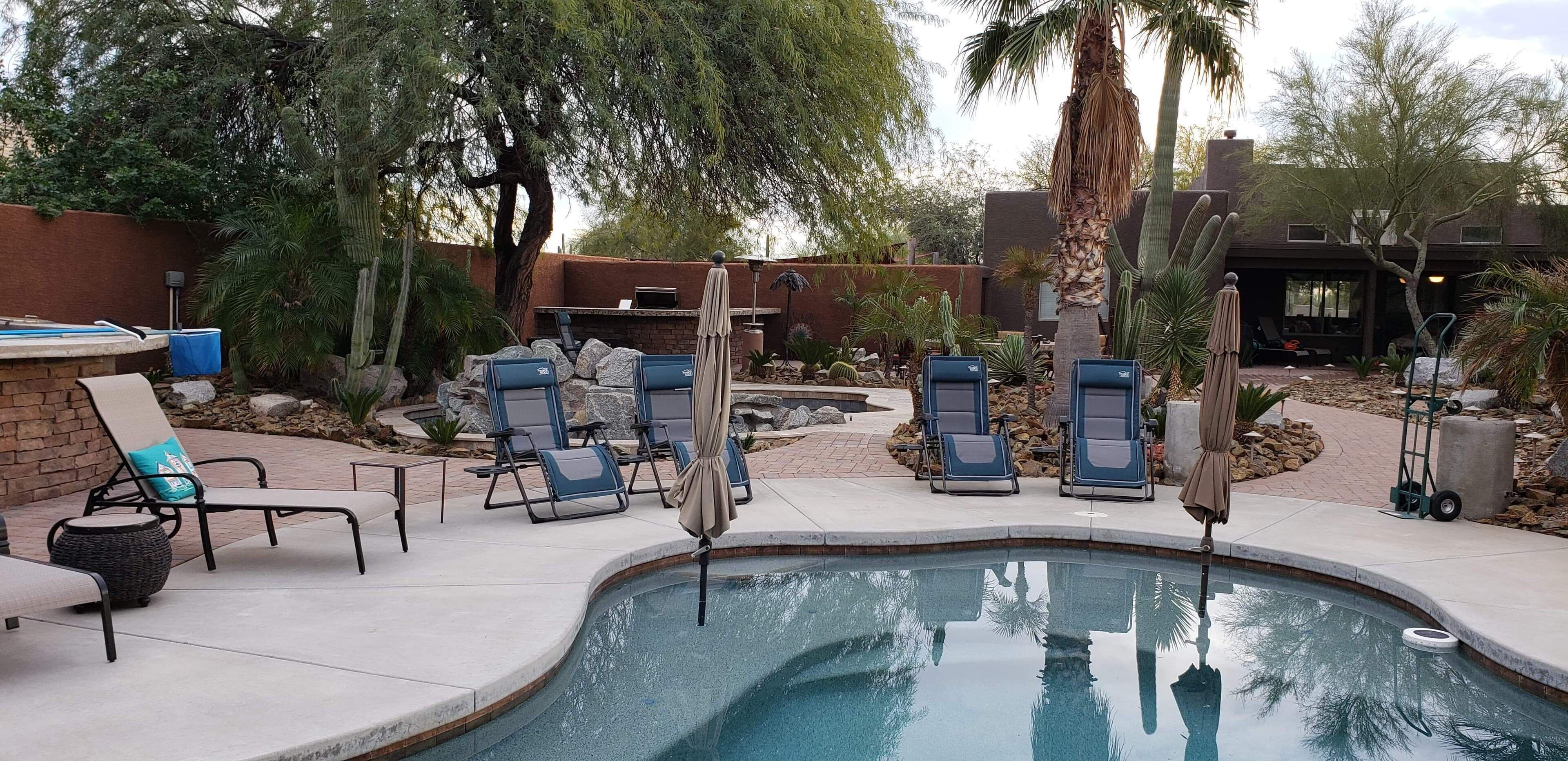 Un espace piscine comprenant des chaises longues, une petite piscine et une terrasse avec un mur en briques et des cactus.